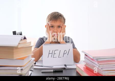 Müde frustrierte Junge sitzt am Tisch, seine Hausaufgaben zwischen Haufen von Büchern. Word Help ist auf offenem Notizbuch geschrieben Stockfoto