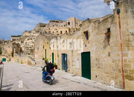 Motorradfahrer in Helmen, die auf Steinstraßen in Matera mit Blick auf das historische Zentrum Sasso Caveoso der alten antiken Stadt Sassi di Mate fahren Stockfoto