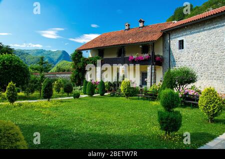 Malerischer Hof des Klosters von Moraca mit grünen Rasen, Blumen und Gebäuden mit roten Ziegeldächern vor blauem Himmel, Montenegro Stockfoto