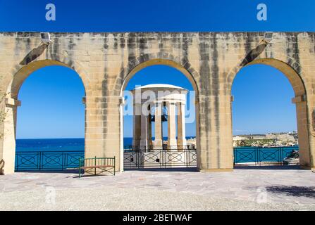 Belagerung des Zweiten Weltkriegs Bell war Memorial durch die Bögen in den Lower Barrakka Gardens, Valletta, Malta Stockfoto