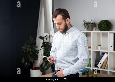 Thema Office Business. Hübscher junger kaukasischer Mann Selbstsicher und stark mit Bart in helles Zimmer auf Arbeitsplatz. stilvoll Hemd Stockfoto