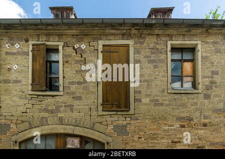 Altes baufällig Haus mit einer Scheune aus hellem Sandstein mit mediterranem Flair unter blauem Himmel und Sonnenschein mit gebrochenen Fensterscheiben und Holz Stockfoto