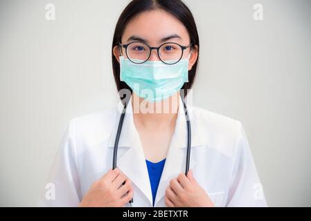 Studio Portrait Vorderseite Gesicht schöne asiatische junge Frau Arzt mit Stethoskop in weiß uniform tragen Brille und grüne Maske Corona Virus fo zu schützen Stockfoto