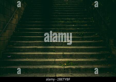 Weite Treppe in einem Park aus Naturstein mit einem Handlauf aus rostfreiem Stahl im dunklen Licht mit einer gruseligen und gruseligen Aura wie in einem Thriller Stockfoto