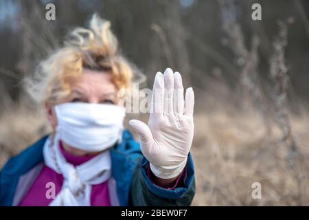 Eine ältere Frau in einer medizinischen Schutzmaske und Gummihandschuhen Gesten stoppen Coronavirus. Stockfoto