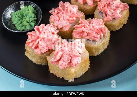 Sushi-Brötchen mit roter Mayonnaise-Sauce auf schwarzem Teller serviert. Nahaufnahme des Fotos Stockfoto