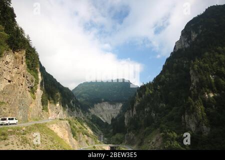 Eine lange kurvenreiche Straße, die durch die Berge absteigt. Wolken auf dem Gipfel des Berges. Stockfoto