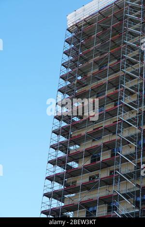 Hohe Wohnung Haus in Bau, raues Gebäude durch Gerüste und Schutznetz abgedeckt. Blauer Himmel im Hintergrund in Schlieren Schweiz Stockfoto