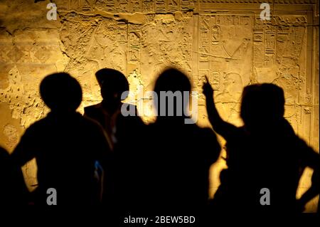 Eine Gruppe von nicht erkennbaren Touristenarcheologen, die in Silhouette vor altägyptischen Hieroglyphen stehen Stockfoto