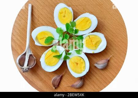 Gekochte Eier mit Rucola-Spigs und Knoblauchzehen auf einem Schneidebrett Stockfoto