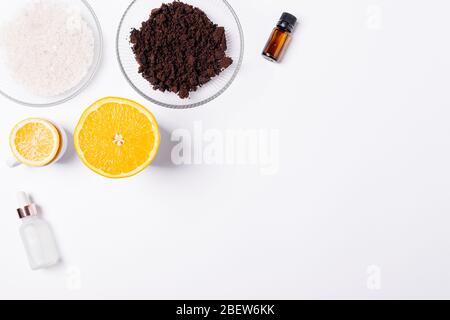 Bio-Zutaten für selbstgemachte kosmetische Körperpeeling aus gemahlenem Kaffee, Meersalz, ätherischem Öl und frischen Zitrusfrüchten auf weißem Hintergrund mit Kopierrau Stockfoto