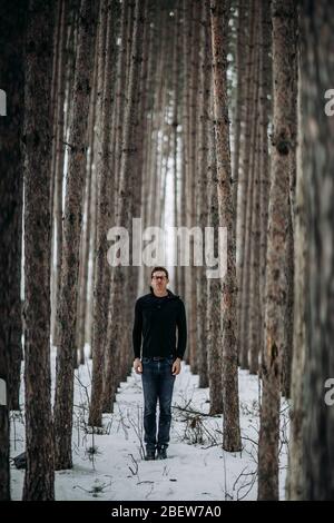 Der junge Mann steht hoch im schneebedeckten Pinienwald in Maine Stockfoto