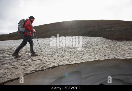 Frau überquert Schneefeld auf dem Laugavegur Wanderweg Stockfoto