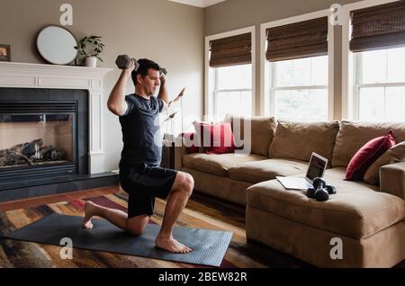 Mann, der mit Gewichten zu Hause mit Online-Übungsprogramm. Stockfoto