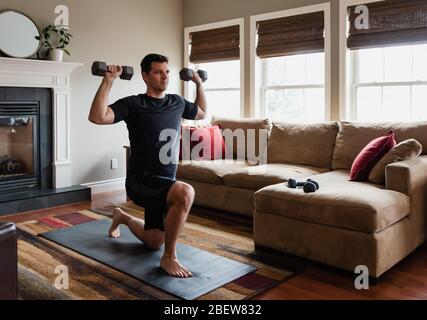 Fit Mann zu Hause mit Handgewichten in seinem Wohnzimmer trainieren. Stockfoto