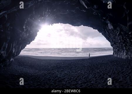 Blick auf den Menschen am Strand bei Sonnenuntergang am Meer von Basalthöhle, Reynisfjara, Island Stockfoto