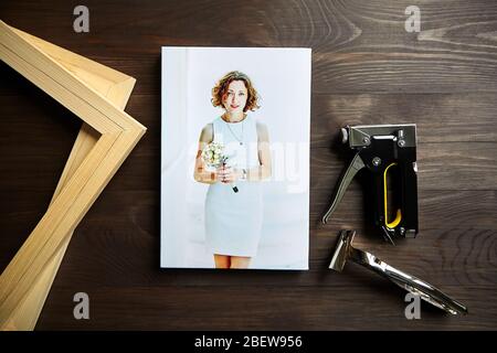 Fotografie auf Leinwand gedruckt. Porträt einer jungen Frau. Foto, Trage Bars, Stapelpistole und Leinwand Zange auf braunen Holztisch Stockfoto