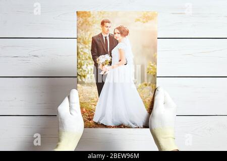 Foto eines Hochzeitspaares auf Leinwand gedruckt. Männliche Hände in weißen Handschuhen halten ein Foto mit Galerie-Verpackung auf Trage-Bar Stockfoto