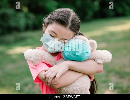 Stress kleines Mädchen hält Spielzeug Bär in medizinischen Schutzmaske Stockfoto