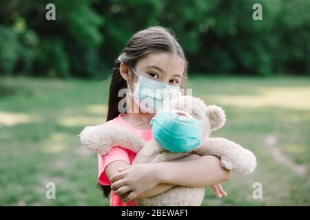 Stress kleines Mädchen hält Spielzeug Bär in medizinischen Schutzmaske Stockfoto