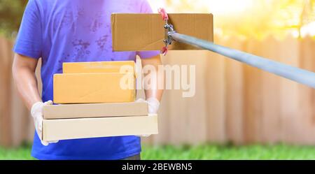 Lieferer hält Boxen mit Gummihandschuhen. Online-Shopping und kostenlose Lieferung nach Hause. Soziale Distanz und zu Hause bleiben sicher bleiben. Stockfoto