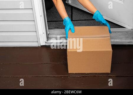 Eine Person, die Handschuhe trägt und eine Lieferkiste von einem Hauseingang abholt Stockfoto