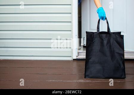 Eine Person, die Handschuhe trägt und eine Lebensmitteltasche von einem Hauseingang abholt Stockfoto