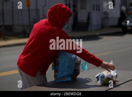 Chelsea, Massachusetts, USA. April 2020. Chelsea, Massachusetts, ist der am stärksten betroffenen Bereich des Staates während COVID-19, Corona Virus. Eine überwiegend lateinamerikanische Gemeinschaft, die sich den Luxus sozialer Distanz nicht leisten kann. Die Stadt hat eine Bevölkerung von 40,000 Menschen in einem 2 Quadratmeilen Radius. 80% der Bevölkerung gelten als wichtige Arbeitskräfte, wie Supermarktmitarbeiter, Transitmitarbeiter usw. das Chelsea-Schulsystem verteilt täglich Frühstück und Mittagessen an Bedürftige. Eine Frau sammelt Nahrung. Kredit: Allison Dinner/ZUMA Wire/Alamy Live News Stockfoto