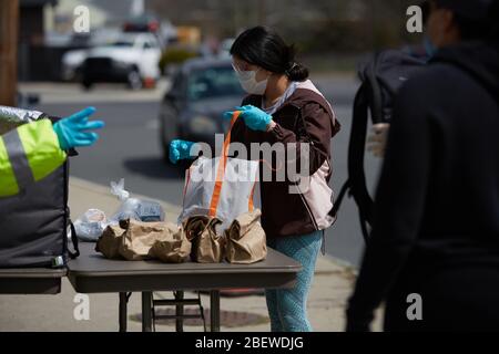 Chelsea, Massachusetts, USA. April 2020. Chelsea, Massachusetts, ist der am stärksten betroffenen Bereich des Staates während COVID-19, Corona Virus. Eine überwiegend lateinamerikanische Gemeinschaft, die sich den Luxus sozialer Distanz nicht leisten kann. Die Stadt hat eine Bevölkerung von 40,000 Menschen in einem 2 Quadratmeilen Radius. 80% der Bevölkerung gelten als wichtige Arbeitskräfte, wie Supermarktmitarbeiter, Transitmitarbeiter usw. das Chelsea-Schulsystem verteilt täglich Frühstück und Mittagessen an Bedürftige. Eine Frau sammelt Nahrung. Kredit: Allison Dinner/ZUMA Wire/Alamy Live News Stockfoto