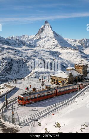 Gornergrat, Zermatt, Schweiz - 12. November 2019: Rote Seilbahn auf der Schneerbahn an der Bergstation mit Touristen und Matterhorn Summit in wi Stockfoto