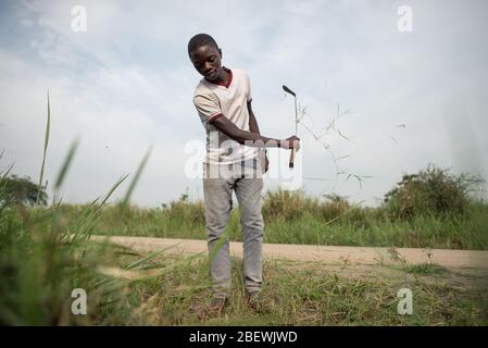 Katwe / Uganda - 25. Oktober 2016: Afrikanischer schwarzer junger Mann, der mit einer Machete Gras schneidet und am Straßenrand des Queen Elisabeth Nationalparks arbeitet Stockfoto