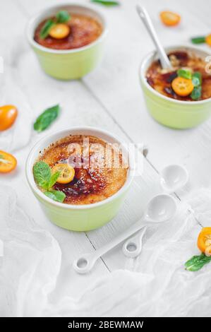 Creme brulee Dessert mit Minze und Kumquat auf weißem Holzhintergrund. Stockfoto