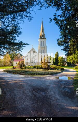 Blick auf die Evandale Kirche und ihren spektakulären Turm, eingerahmt von großen Bäumen in der kulturell bedeutenden Stadt Evandale in Tasmanien. Stockfoto