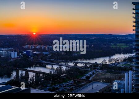 Die Sonne geht über den Colorado River hinaus und über den Colorado River mit Brücken, in der Nähe der Innenstadt von Austin, Texas, mit modernen Wolkenkratzer-Gebäuden im Vordergrund Stockfoto