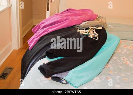 Stapel von Frauenkleidung auf dem Bett vor dem leeren Schrank sortiert werden Stockfoto