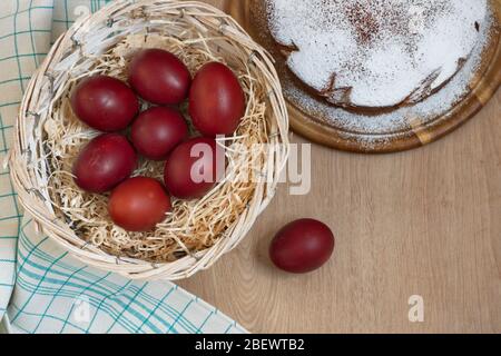 Direkt über Schuss Ostereier in Korb mit Stroh und Kuchen auf Holzhintergrund Stockfoto
