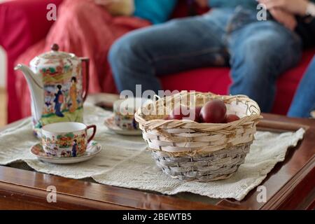 Ostereier im Korb auf dem Tisch mit Teekanne und Teebecher - unerkennbare Menschen sitzen auf dem Sofa Stockfoto