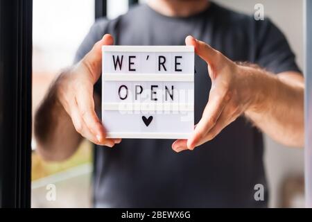 Ende der Quarantäne. Mann mit Leuchtkasten mit Grußtext Wir sind offen in seinen Händen. Hotel, Café, lokaler Shop, Service-Besitzer begrüßen Gäste af Stockfoto