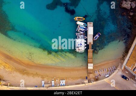 Antenne eines schönen Strandes mit Boot Peer. Ein Kai, der von einer Drohne in Griechenland auf Korfu geschossen wurde. Boote und ein lebhaftes türkisfarbenes mittelmeer Stockfoto