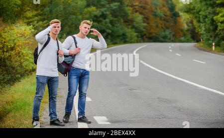 Budget Reisende. Männer Rucksäcke zu Fuß zusammen auf der Straße. Zwillinge zu Fuß entlang der Straße. Abenteuer und Entdeckung. Mann mit Rucksack Anhalter auf der Straße. Sommerurlaub. Automatischer Stopp für Reisende. Stockfoto