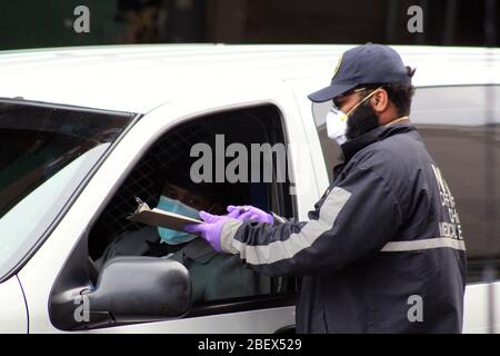 New York, New York, USA. April 2020. Dieser Bestatter in einem grauen Anzug, Gesicht maskiert und Kopf trägt einen Hut, Schaut hinter das Steuer seines Leichenwagens auf die Transportgenehmigung, die ihm ein Agent des New York City Medical Office vorlegt, um einen Patienten aus dem Körper zu holen, bevor er den Verstorbenen in die Beerdigungshäuser fährt. Der Leichenmörder wartet vor dem Eingang des größten provisorischen Leichenhauses außerhalb des Bellevue Hospital inmitten des Coronavirus-Ausbruchs in New York auf seine ständige hin- und Herbiegung von Beerdigungswagen. Quelle: Marie Le BLE/ZUMA Wire/Alamy Live News Stockfoto