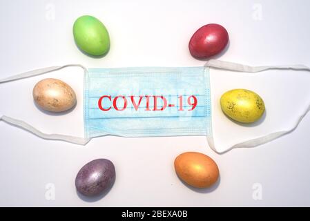 Viele farbige ostereier liegen um medizinische Maske auf dem weißen Hintergrund mit dem Text. Coronavirus Covid-19. Konzeptfoto. Ostern 2020. Stockfoto