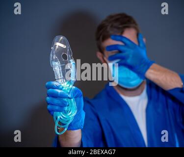 COVID-19 Ausbruch. Erschöpfter Arzt mit nichtinvasivem Beatmungsgerät. Medizinische Behandlung und Mangel an Ausrüstung für Coronavirus-infizierte Patienten mit S Stockfoto
