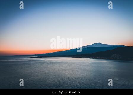 Panoramablick auf den schneebedeckten Ätna und das friedliche Wasser des Ionischen Meeres bei Sonnenuntergang von Taormina, Sizilien Stockfoto