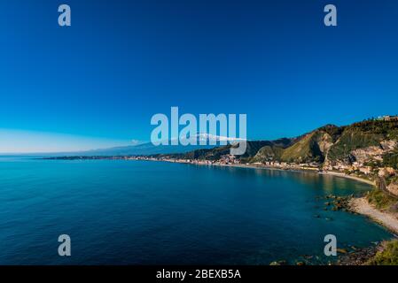 Herrlicher Blick auf den schneebedeckten Ätna und die weite Bucht von Giardini Naxos (erste griechische Kolonie Siziliens), aufgenommen von Capo Taormina, Sizilien Stockfoto