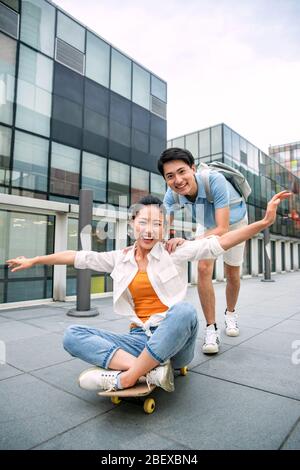 Der junge Mann schiebt sich auf der Freundin des Skateboards nach vorne Stockfoto