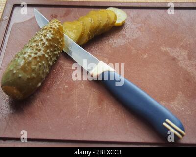 Auf dem Schneidebron befinden sich eine Gurke und ein Messer. Die Gurke wird in Scheiben geschnitten. Stillleben Stockfoto