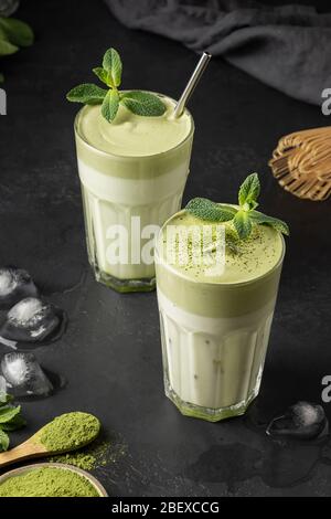 Zwei Gläser Dalgona Iced Matcha Tee. Kalte Milch und Schlagmatcha-Tee mit weißen Eiern auf schwarzem Hintergrund. Schmackhaftes virales Getränk in der Zeit Selbstisolierung. Stockfoto