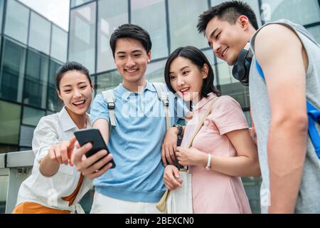 Draußen vier Studenten beobachten Handy Stockfoto