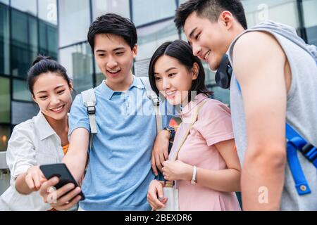 Draußen vier Studenten beobachten Handy Stockfoto